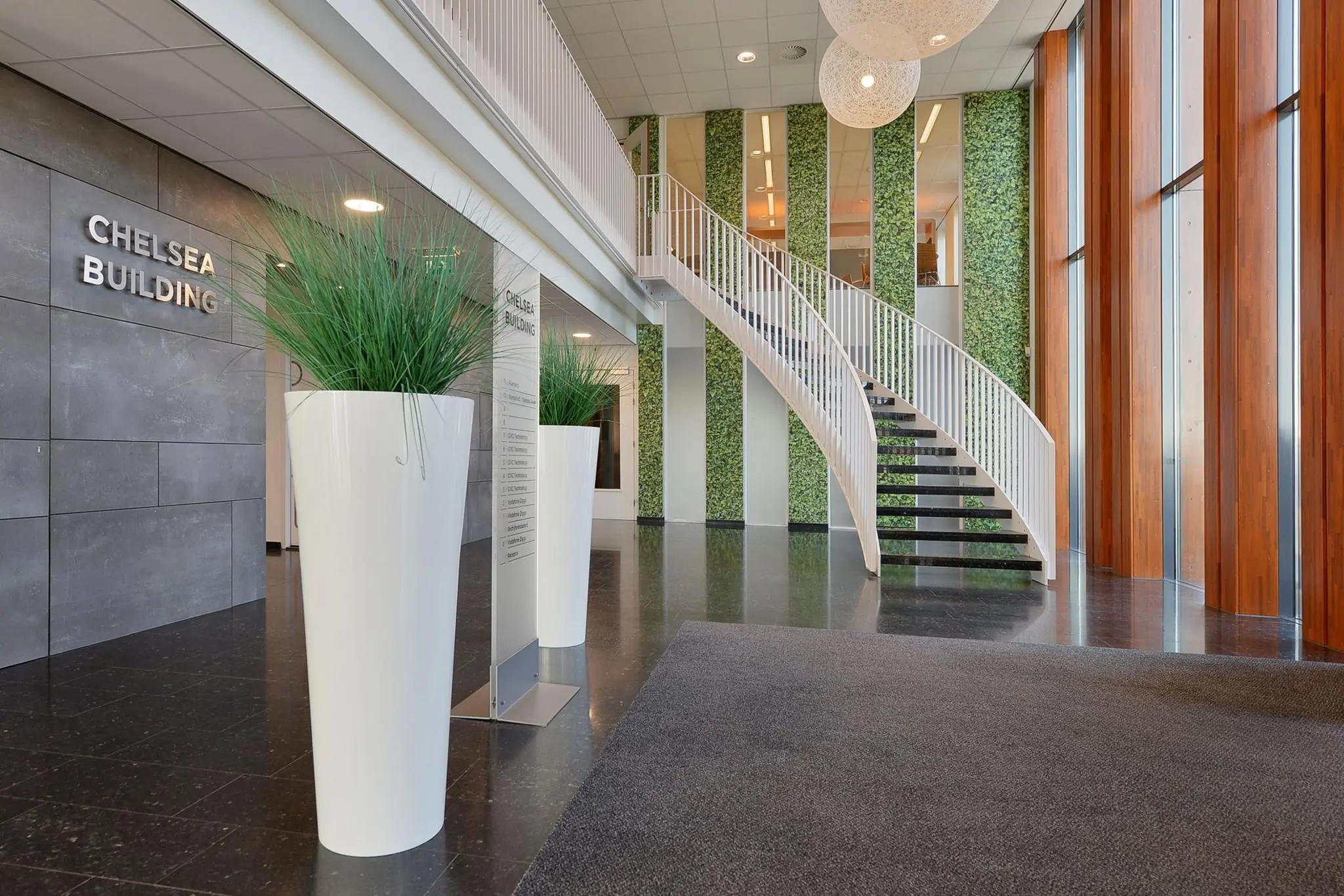 Moderne entreehal van het Chelsea Building aan de Laan van Zuid Hoorn met een witte wenteltrap, hoge plantenbakken en grote ramen.